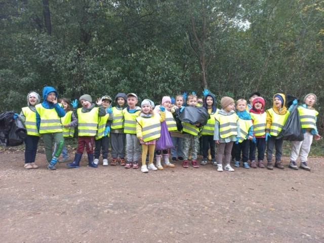 Dzieci stoją i pokazują zebrane odpady w lesie.
