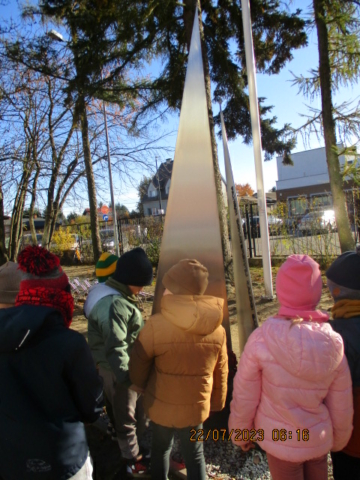 Dzieci stoją przed pomnikiem załogi samolotu B17 na terenie Szkoły Podstawowej w Dziekanowie Leśnym