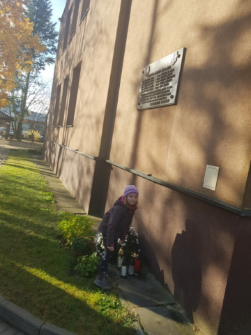 Dziewczyna stawia znicz przy tablicy pamiątkowej